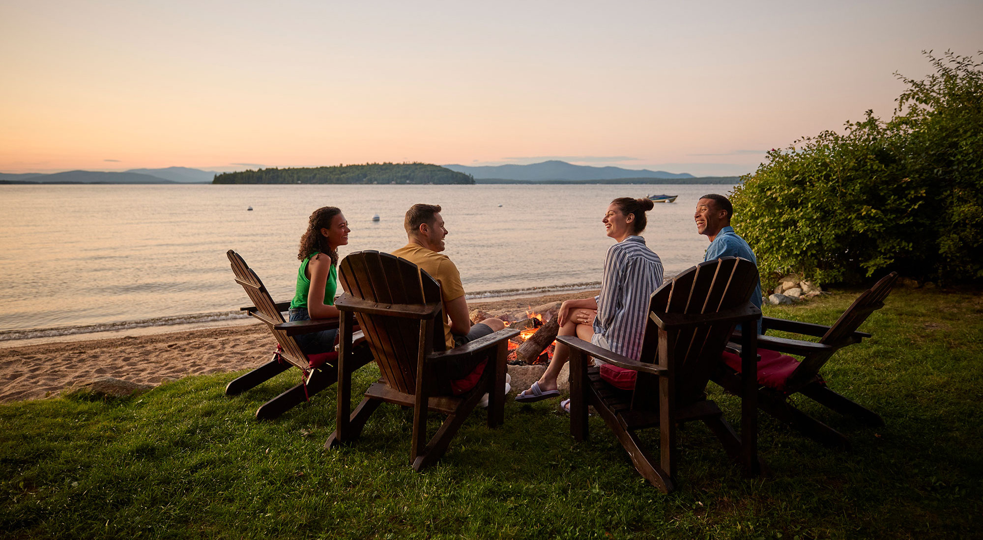 Couples enjoying a bonfire during a sunset on Lake Winnipesaukee in New Hampshire