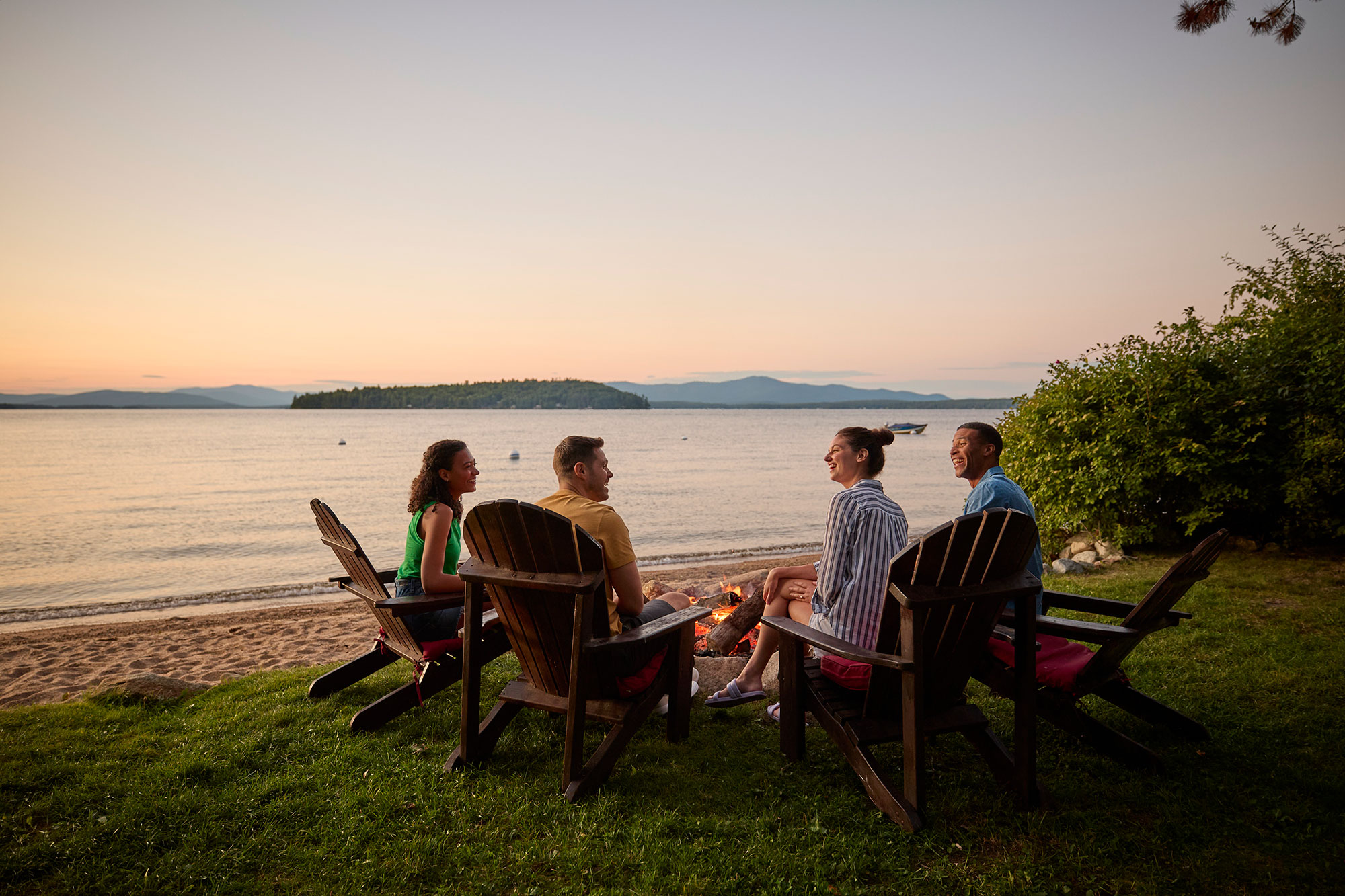 Couples enjoying a bonfire during a sunset on Lake Winnipesaukee in New Hampshire