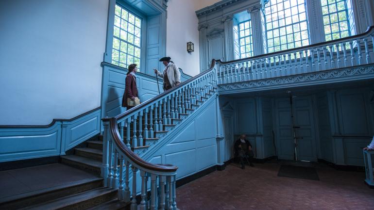 2 colonial gentlemen conversing on a staircase
