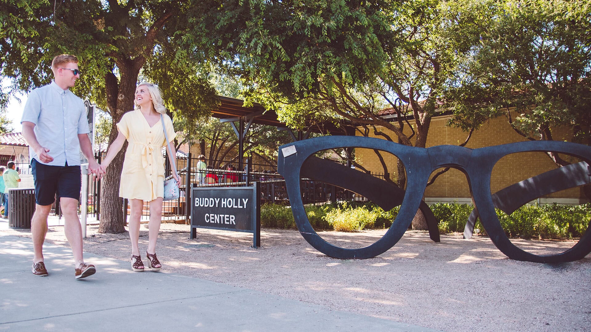 Leute gehen am Buddy Holly Center in Lubbock, Texas an der Statue von Buddy Hollys Brille vorbei